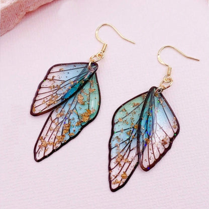 des boucles d'oreilles en forme d'ailes de fées colorées et toute pailletées. Elles semblent sortis d'un conte