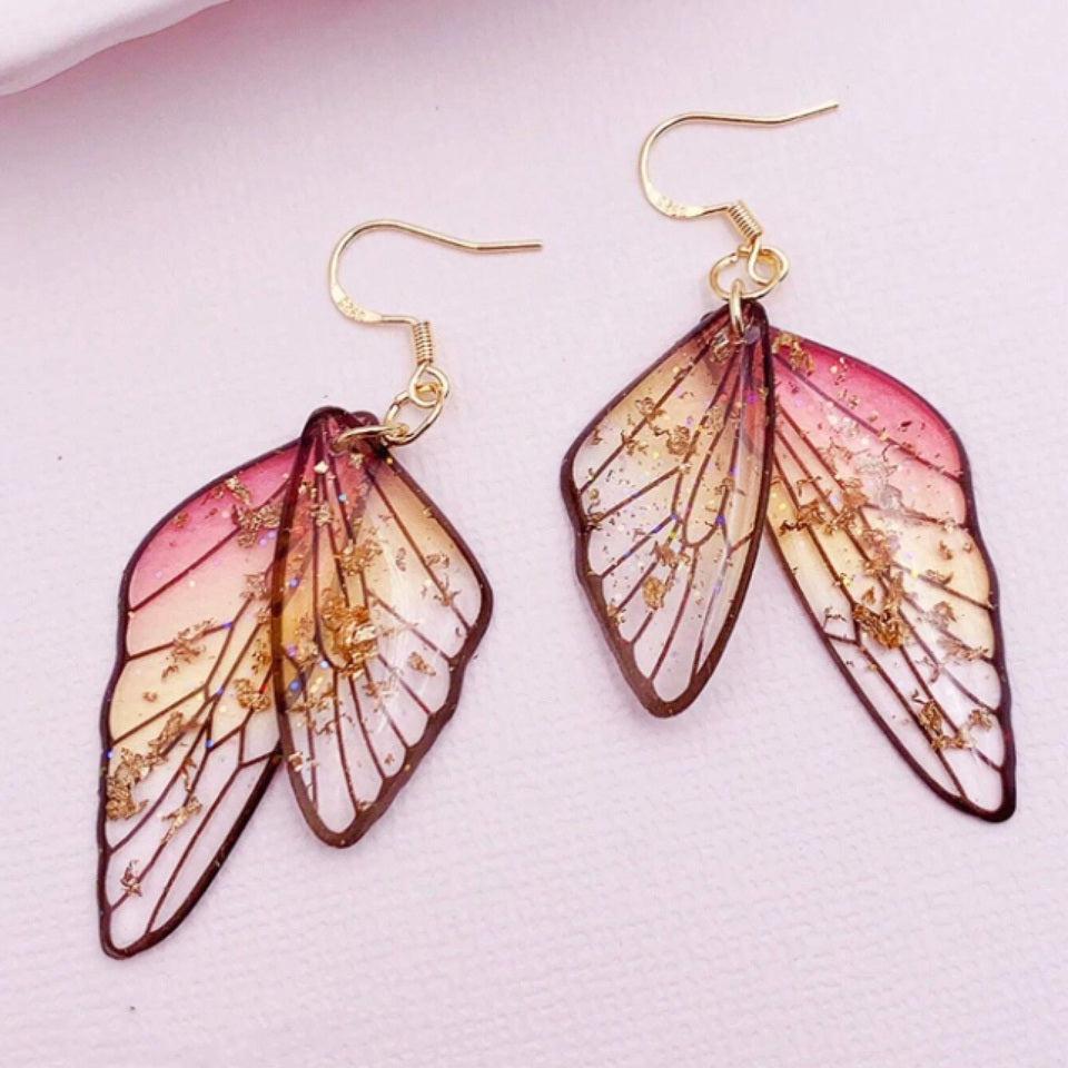 des boucles d'oreilles en forme d'ailes de fées colorées et toute pailletées. Elles semblent sortis d'un conte