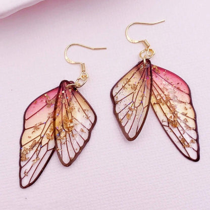 des boucles d'oreilles en forme d'ailes de fées colorées et toute pailletées. Elles semblent sortis d'un conte