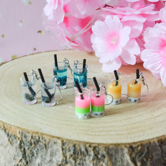 des boucles d'oreilles en forme de bubble tea de couleurs différentes. Certaines sont pailletées. Elles ont une paille pour plus de réalisme.
