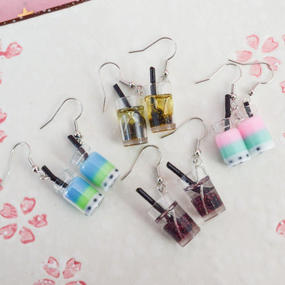 des boucles d'oreilles en forme de bubble tea de couleurs différentes. Certaines sont pailletées. Elles ont une paille pour plus de réalisme.