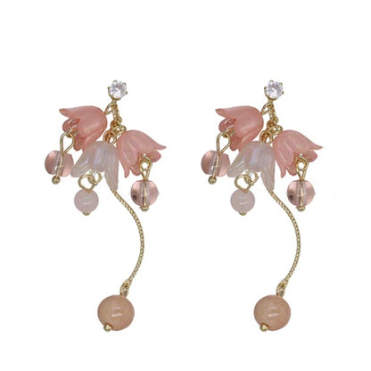 une paire de boucles d'oreilles composées de trois fleurs pendantes d'où pend une perle rose ou blanche, d'une tige courbée dorée avec une perle rose et blanche et d'un strass scintillant.