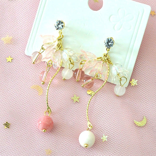 une paire de boucles d'oreilles composées de trois fleurs pendantes d'où pend une perle rose ou blanche, d'une tige courbée dorée avec une perle rose et blanche et d'un strass scintillant.