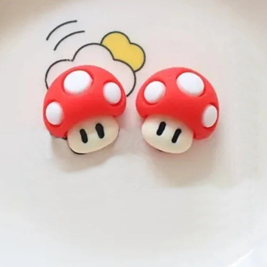 une paire de boucles d'oreilles en forme de champignon rouge à pois blancs, inspirées du jeu vidéo Mario.
