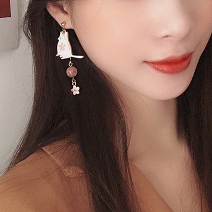 des boucles d'oreilles asymétriques avec un chat blanc et une perle rose d'un côté. De l'autre côté, il y  a un éventail avec une chainette ornée de perles blanches et d'une petite fleur de sakura.