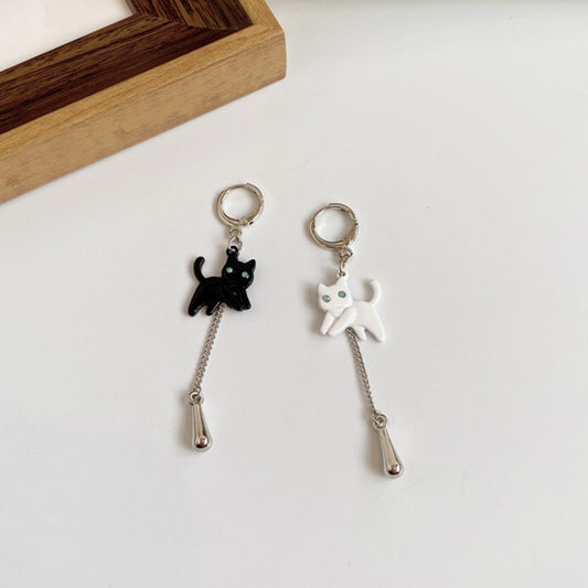 une paire de boucles d'oreilles dépareillées pour un style mignon et original. D'un côté, un chat noir et de l'autre, un chat blanc. Les deux chats semblent vouloir s'amuser. Au bout des chat est suspendu une breloque en forme de goutte argentée.