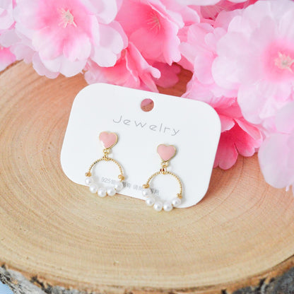 des boucles d'oreilles composées d'un coeur rose et d'une ronde de perles blanches pour un style romantique
