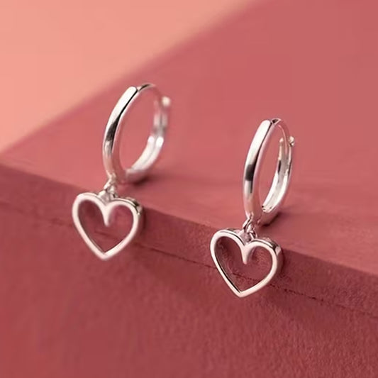 des petites créoles argentés d'où pendent un petit coeur. Style romantique, minimaliste, épuré et élégant.