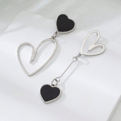 une paire de boucles d'oreilles asymétriques en forme de gros coeurs noirs pour un look romantique et mignon