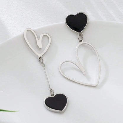 une paire de boucles d'oreilles asymétriques en forme de gros coeurs noirs pour un look romantique et mignon