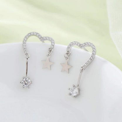une paire de boucles d'oreilles en forme de coeur tout en strass. A chaque bout du coeur, est suspendu une étoile et un strass brillant.