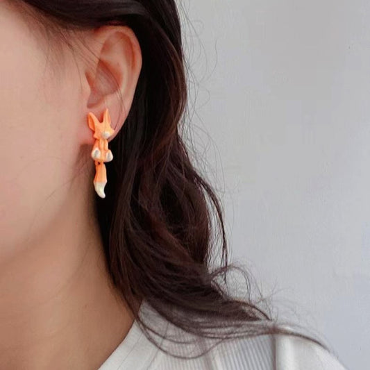 des boucles d'oreilles composées de deux renards : un blanc et un roux. Leur queue est pendante et le design est très mignon