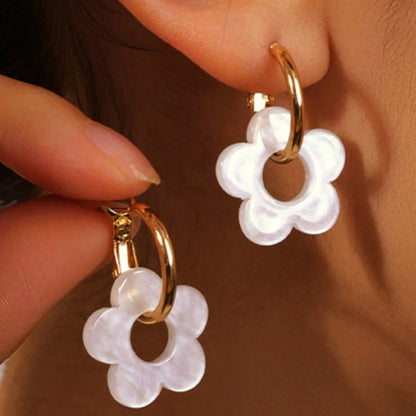 une paire de boucles d'oreilles créoles dorées dans lesquelles se trouve une jolie fleur blanche en acrylique. Style bohème chic