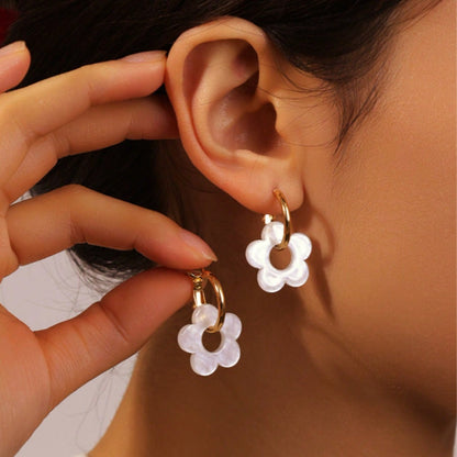 une paire de boucles d'oreilles créoles dorées dans lesquelles se trouve une jolie fleur blanche en acrylique. Style bohème chic