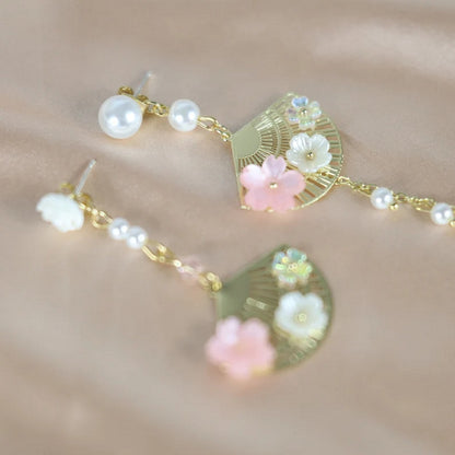 une paire de boucles d'oreilles asymétriques composées d'éventails dorés décorés avec de jolies fleurs de sakura, des perles blanches viennent apporter de l'élégance à l'ensemble.