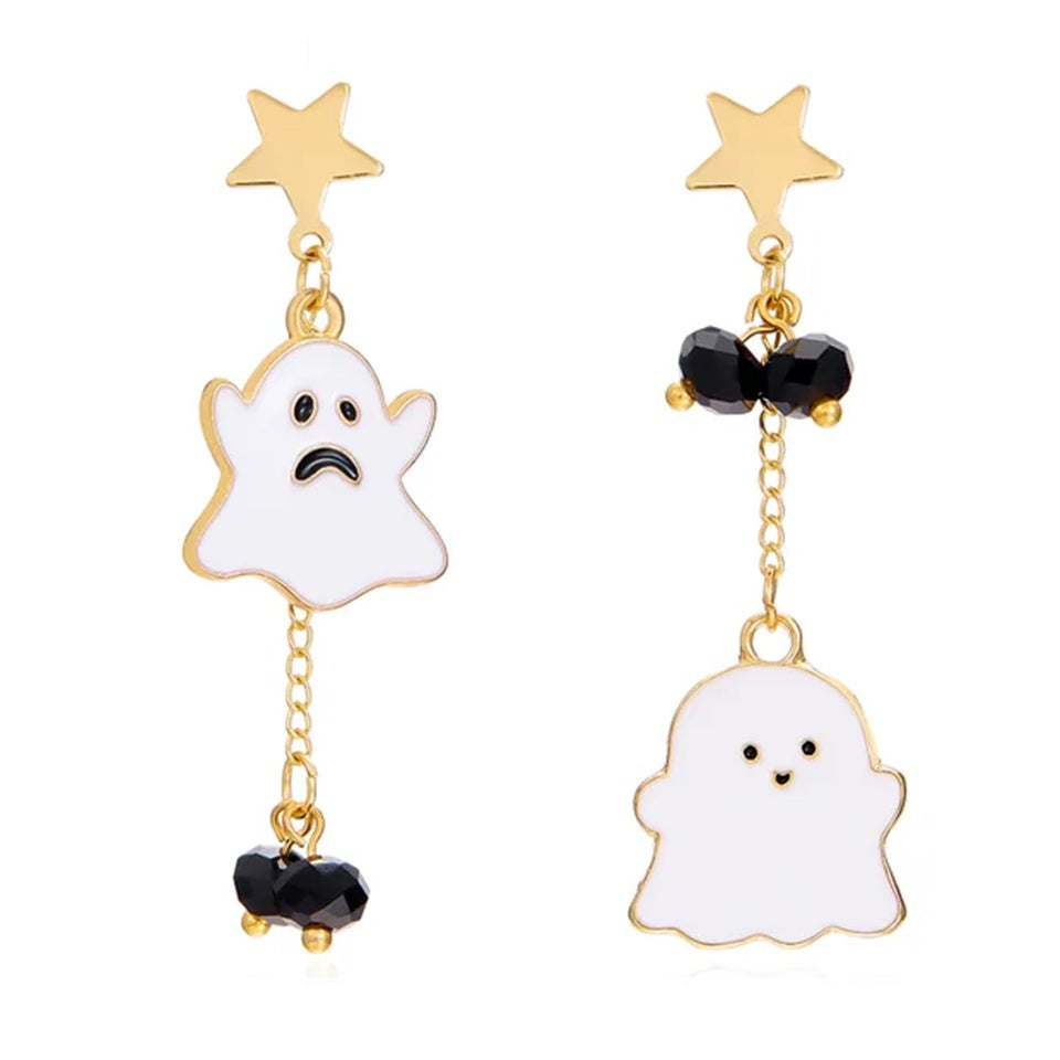 Gros plan sur des boucles d’oreilles asymétriques fantômes kawaii blancs et dorées avec étoiles et perles noires