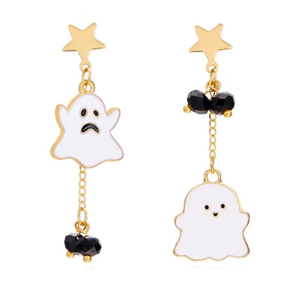 Gros plan sur des boucles d’oreilles asymétriques fantômes kawaii blancs et dorées avec étoiles et perles noires