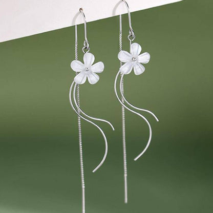 des boucles d'oreilles argentées composées d'une fleur blanche, d'une chaine pendante à l'arrière et de tige courbées devant. Elles évoquent la danse des fleurs
