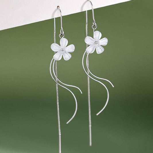 des boucles d'oreilles argentées composées d'une fleur blanche, d'une chaine pendante à l'arrière et de tige courbées devant. Elles évoquent la danse des fleurs