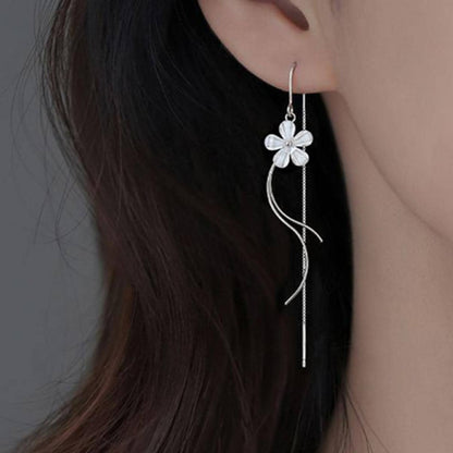des boucles d'oreilles argentées composées d'une fleur blanche, d'une chaine pendante à l'arrière et de tige courbées devant. Elles évoquent la danse des fleurs