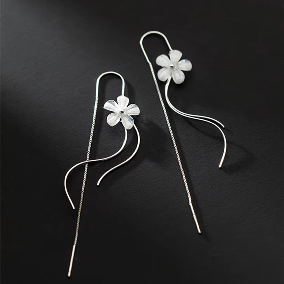 des boucles d'oreilles argentées composées d'une fleur blanche, d'une chaine pendante à l'arrière et de tige courbées devant. Elles évoquent la danse des fleurs