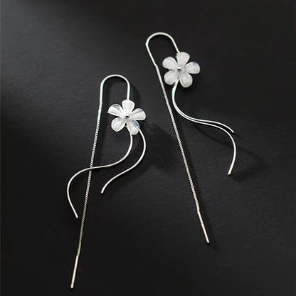des boucles d'oreilles argentées composées d'une fleur blanche, d'une chaine pendante à l'arrière et de tige courbées devant. Elles évoquent la danse des fleurs