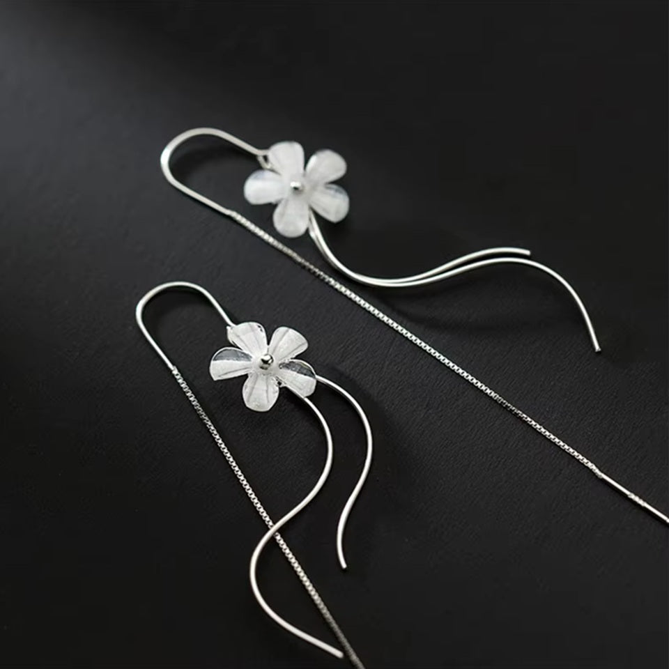 des boucles d'oreilles argentées composées d'une fleur blanche, d'une chaine pendante à l'arrière et de tige courbées devant. Elles évoquent la danse des fleurs