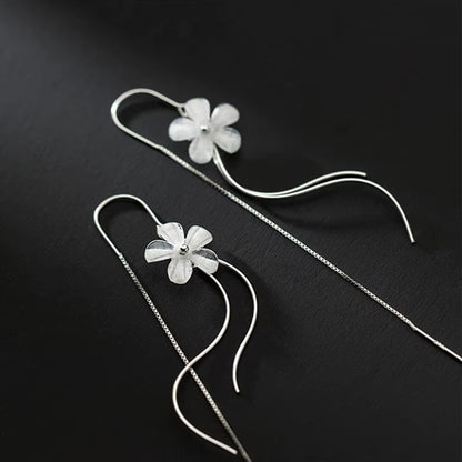 des boucles d'oreilles argentées composées d'une fleur blanche, d'une chaine pendante à l'arrière et de tige courbées devant. Elles évoquent la danse des fleurs