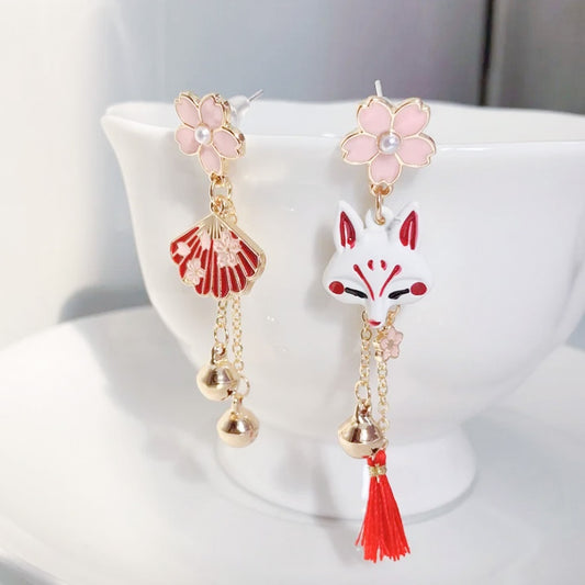 une paire de boucles d'oreilles asymétriques inspirées du folklore japonais. d'un côté un kitsune  avec un petit pompon rouge, de l'autre, un éventail. L'ensemble des couleurs rouge et blanc forment une harmonie parfaite. Des petites clochettes viennent compléter le tout.