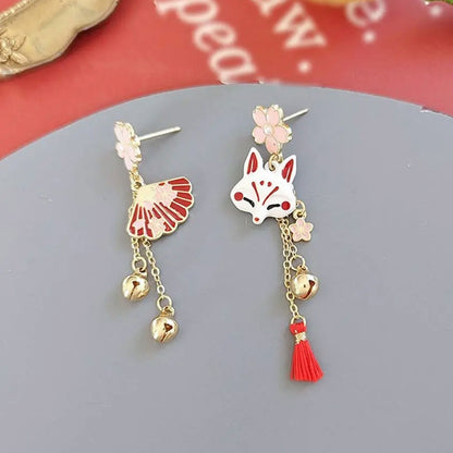 une paire de boucles d'oreilles asymétriques inspirées du folklore japonais. d'un côté un kitsune  avec un petit pompon rouge, de l'autre, un éventail. L'ensemble des couleurs rouge et blanc forment une harmonie parfaite. Des petites clochettes viennent compléter le tout.