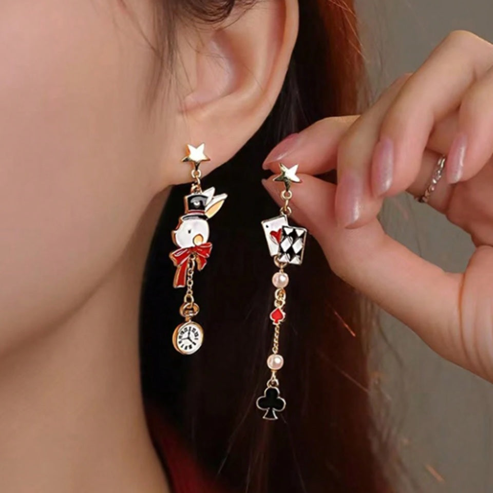 une paire de boucles d'oreilles asymétriques inspirés de l'univers d'Alice aux pays des merveilles. D'un côté un lapin blanc et sa montre, de l'autre, des cartes à jouer et des perles blanches.