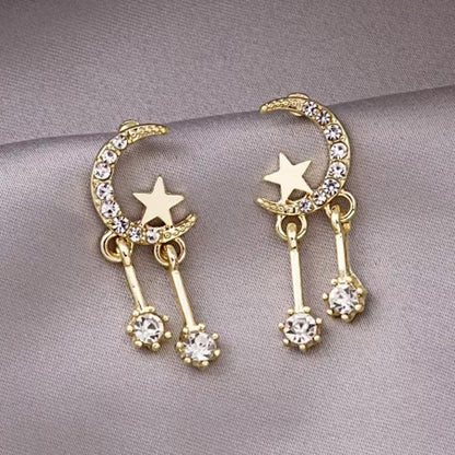 une paire de boucles d'oreilles en forme de lune toute en strass dans laquelle repose une étoile dorée. Deux strass sont suspendus à la lune et apportent encore plus de brillance.