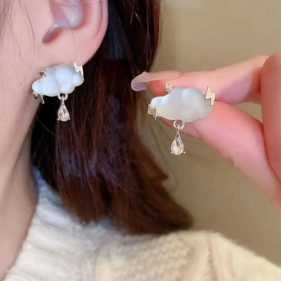 une paire de boucles d'oreilles en forme de nuage transparents d'où pendent un joli strass en forme de goutte. Des éclairs habillent les nuages