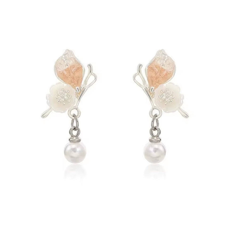 une paire de boucles d'oreilles florale et printanière représentant des papillons d'un rose pâle sur leurs ailes avec une jolie fleur blanche. Une perle blanche suspendu à leurs ailes vient compléter l'ensemble
