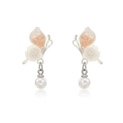 une paire de boucles d'oreilles florale et printanière représentant des papillons d'un rose pâle sur leurs ailes avec une jolie fleur blanche. Une perle blanche suspendu à leurs ailes vient compléter l'ensemble