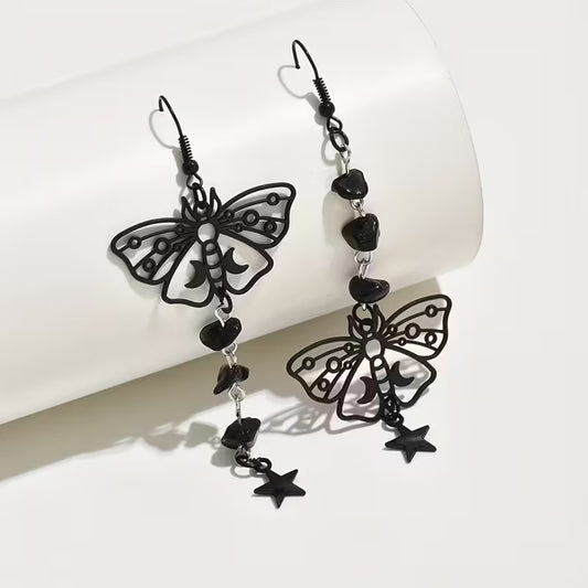 une paire de boucles d'oreilles en forme de papillons noirs orné de croissants de lune. De jolies pierres noires et étoiles pendent le long de la boucle pour un effet mystérieux et ésotérique.