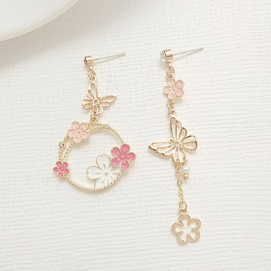 une paire de boucles d'oreilles asymétriques composées d'un papillon doré et de fleurs de sakura rose