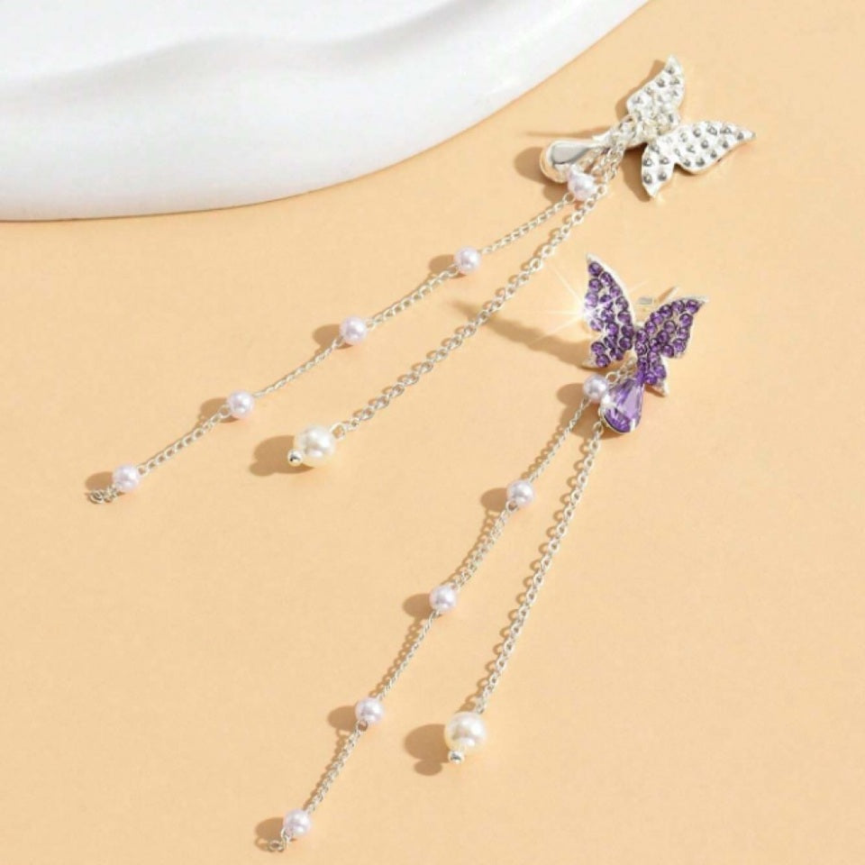 des boucles d'oreilles en forme de papillons violets tout en strass. Des chainettes de perles blanches y sont suspendus