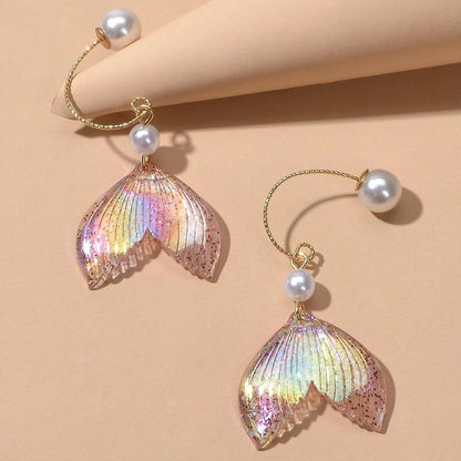 des boucles d'oreilles en forme de queues de sirènes pailletées et roses. De jolies perles blanches viennent ajouter de l'élégance à l'ensemble