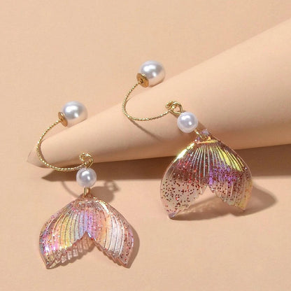 des boucles d'oreilles en forme de queues de sirènes pailletées et roses. De jolies perles blanches viennent ajouter de l'élégance à l'ensemble