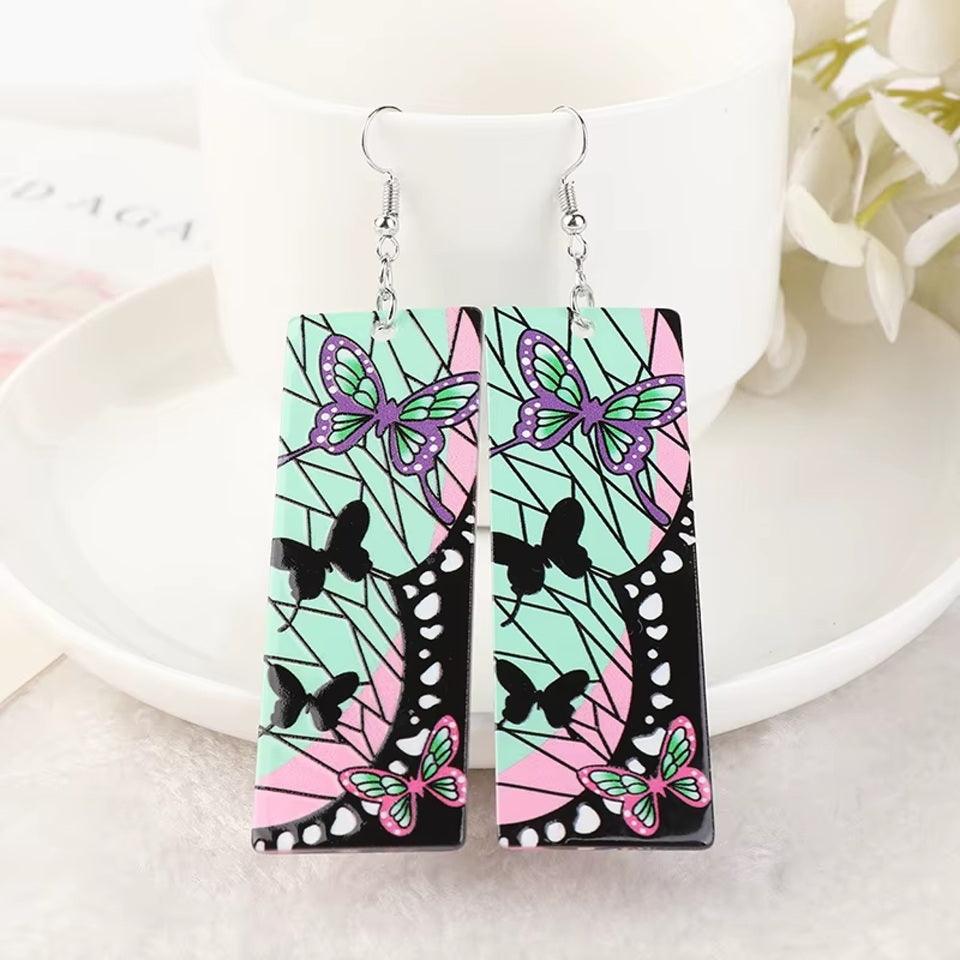 des boucles d'oreilles rectangulaires aux couleurs de Shinobu Kocho du manga Demon Slayer. On retrouve ses signes distinctifs comme les papillons