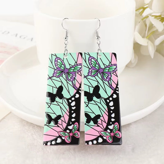 des boucles d'oreilles rectangulaires aux couleurs de Shinobu Kocho du manga Demon Slayer. On retrouve ses signes distinctifs comme les papillons