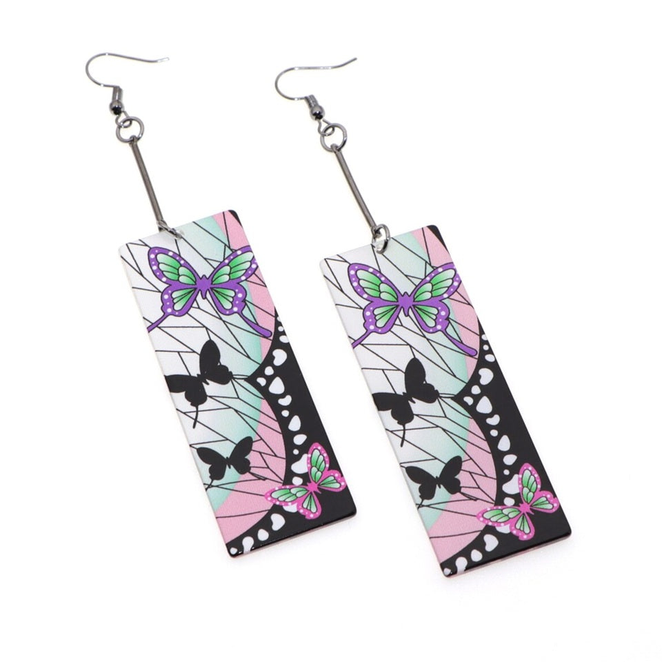 des boucles d'oreilles rectangulaires aux couleurs de Shinobu Kocho du manga Demon Slayer. On retrouve ses signes distinctifs comme les papillons