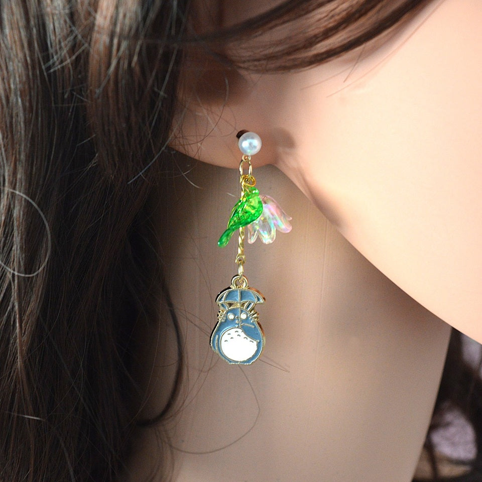 Une paire de boucles d'oreilles asymétriques Totoro qui porte son parapluie, de l'autre côté se trouve une jolie fleur rose et une feuille verte