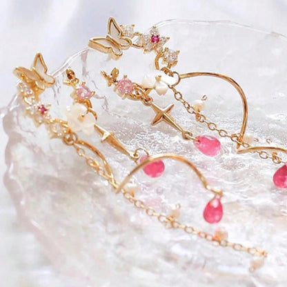 une paire de boucles d'oreilles composées d'une ronde de fleurs blanches et de strass roses, d'un joli papillon blanc, d'où pendent une chaine dorée et une tige torsadée ainsi qu'une douce étoilée dorée. Au bout, il y a des perles en forme de goutte rose. l'ensemble est poétique et féminin.