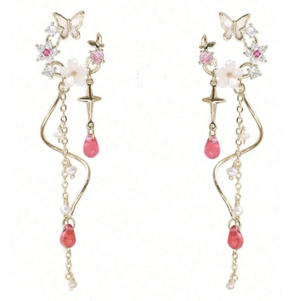 une paire de boucles d'oreilles composées d'une ronde de fleurs blanches et de strass roses, d'un joli papillon blanc, d'où pendent une chaine dorée et une tige torsadée ainsi qu'une douce étoilée dorée. Au bout, il y a des perles en forme de goutte rose. l'ensemble est poétique et féminin.