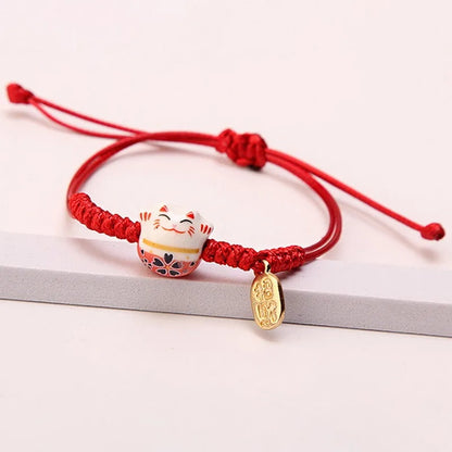 un bracelet en tissu en forme d'un maneki neko coloré. Symbole de chance, de bonne fortune, il est inspiré du style japonais