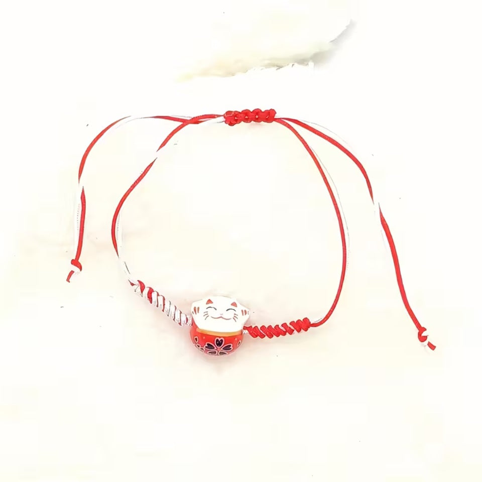 un bracelet en tissu en forme d'un maneki neko coloré. Symbole de chance, de bonne fortune, il est inspiré du style japonais