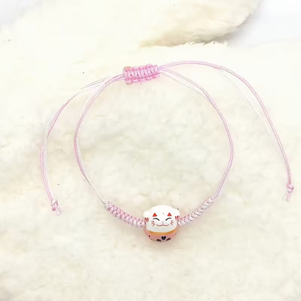 un bracelet en tissu en forme d'un maneki neko coloré. Symbole de chance, de bonne fortune, il est inspiré du style japonais