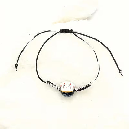 un bracelet en tissu en forme d'un maneki neko coloré. Symbole de chance, de bonne fortune, il est inspiré du style japonais